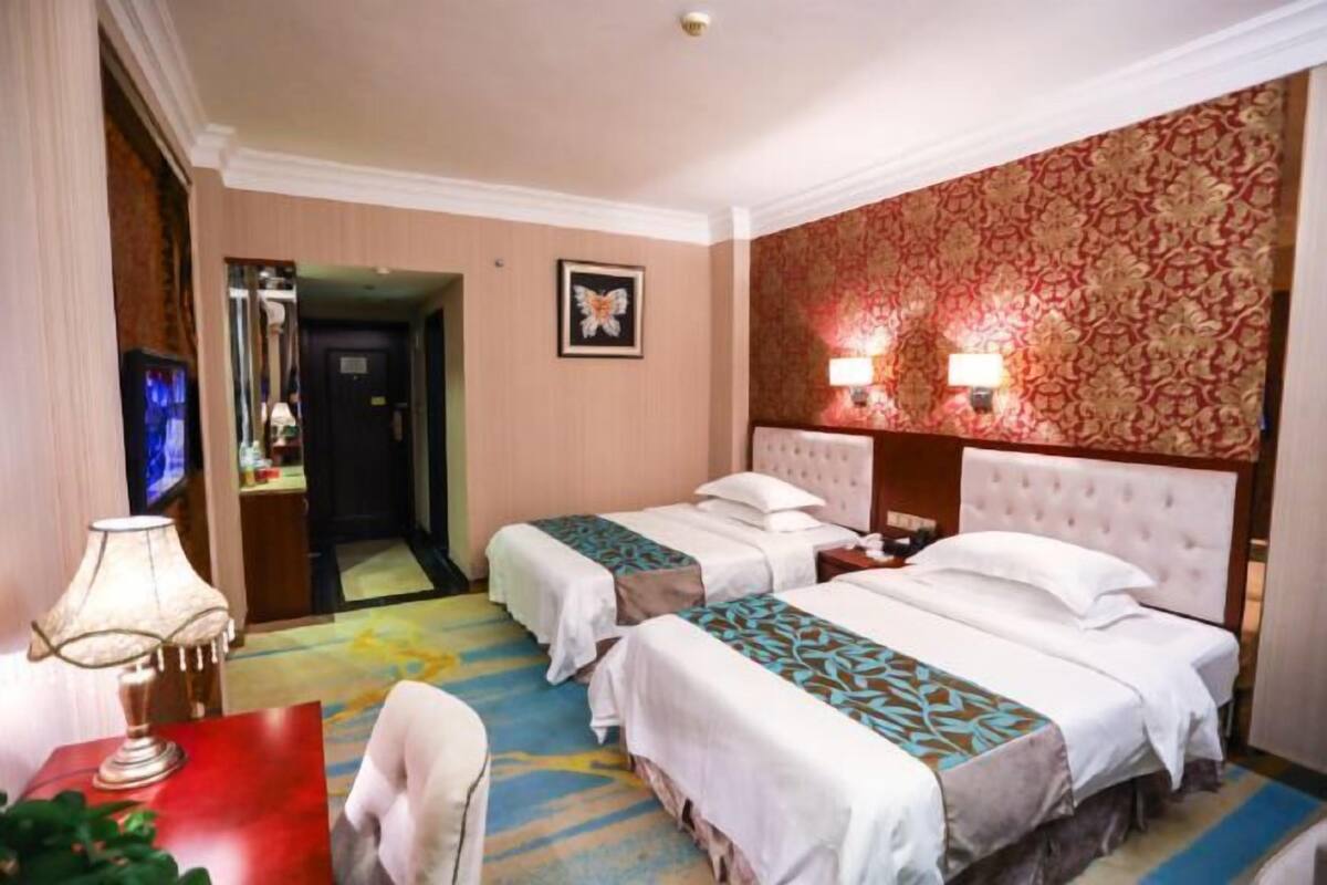 Une chambre d’hôtel avec deux lits, une télévision, un bureau avec une lampe et une moquette à motifs.