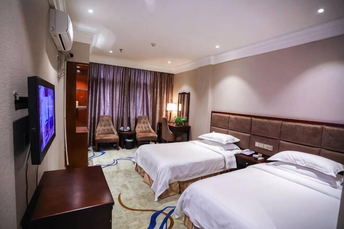 Une chambre d’hôtel avec deux lits, une télévision, un bureau, une chaise, une lampe et un rideau.