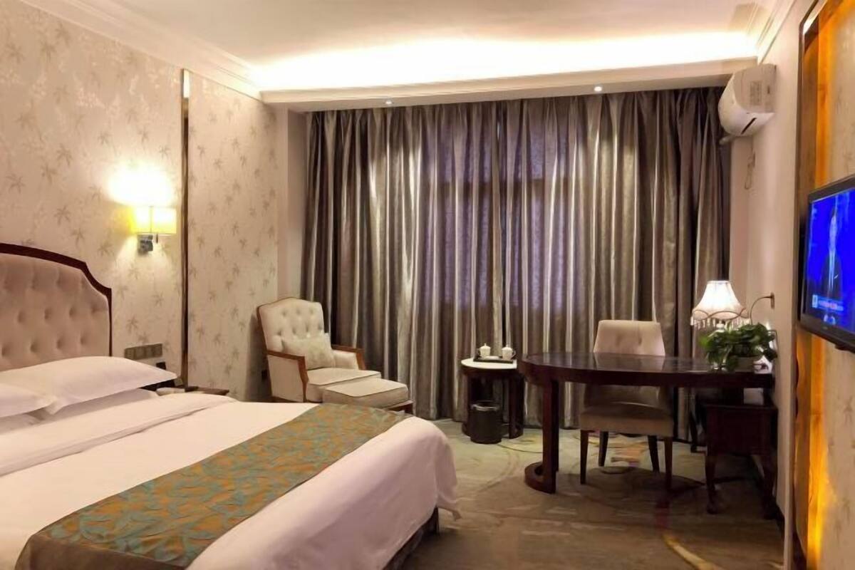 Une chambre d’hôtel avec un lit, une chaise, un bureau, une télévision et des rideaux.