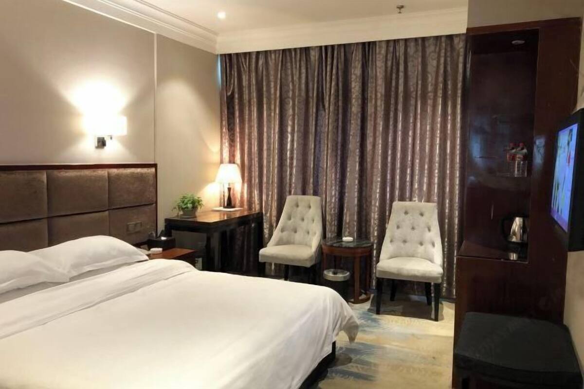 Une chambre d’hôtel avec un grand lit, deux fauteuils, une petite table, un téléviseur et un rideau servant de décor.