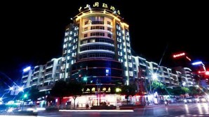 Un hotel de varios pisos con fachada curva, señalización iluminada y un área de entrada bien iluminada.