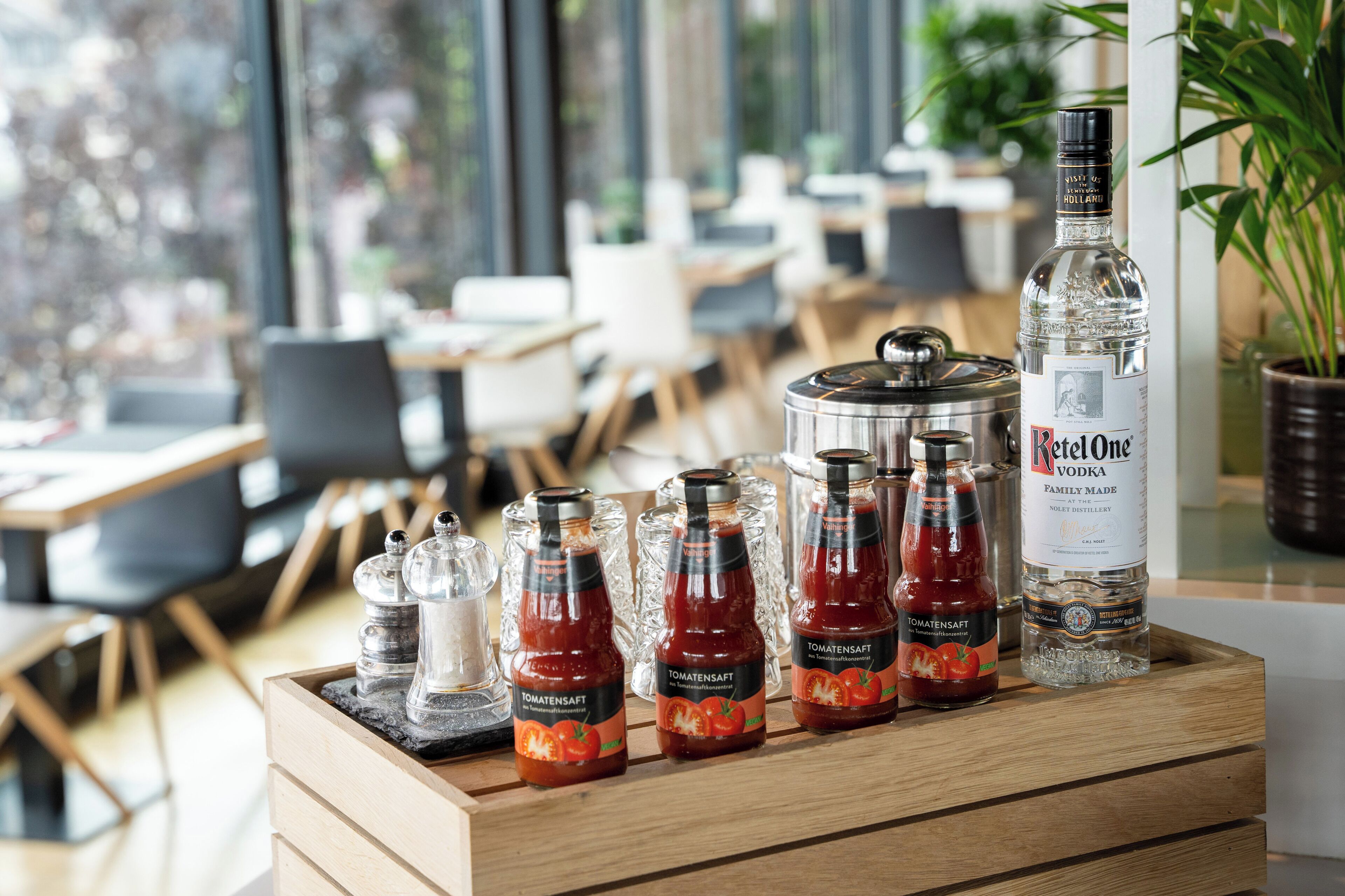 Een houten presentatieblad met flessen Tomatensaft en Rotalone wodka, zout- en peperstrooiers, en een grote pot.