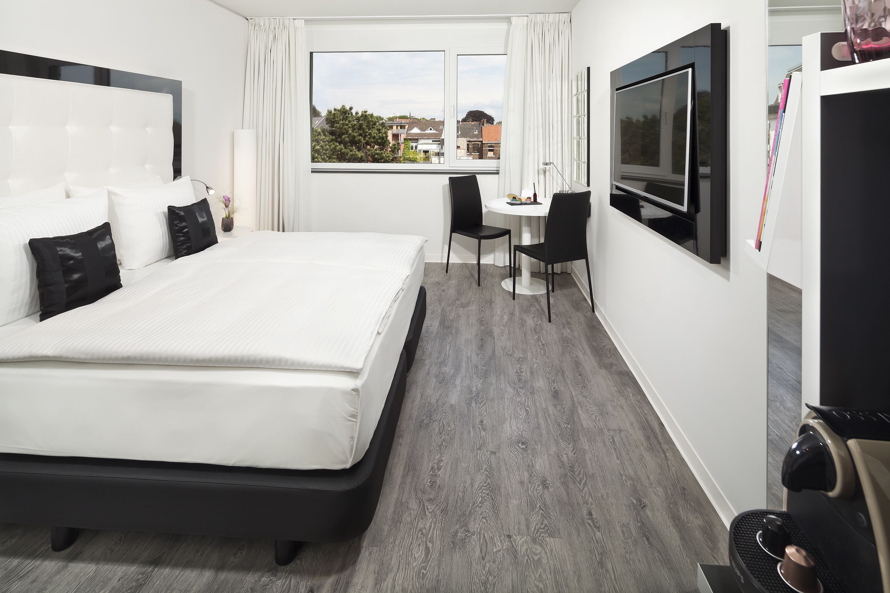 Habitación de hotel moderna con una cama grande, un escritorio, un televisor y vistas a la ciudad.