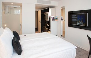 Habitación de hotel con cama, armario, ducha y televisor montado mostrando información.