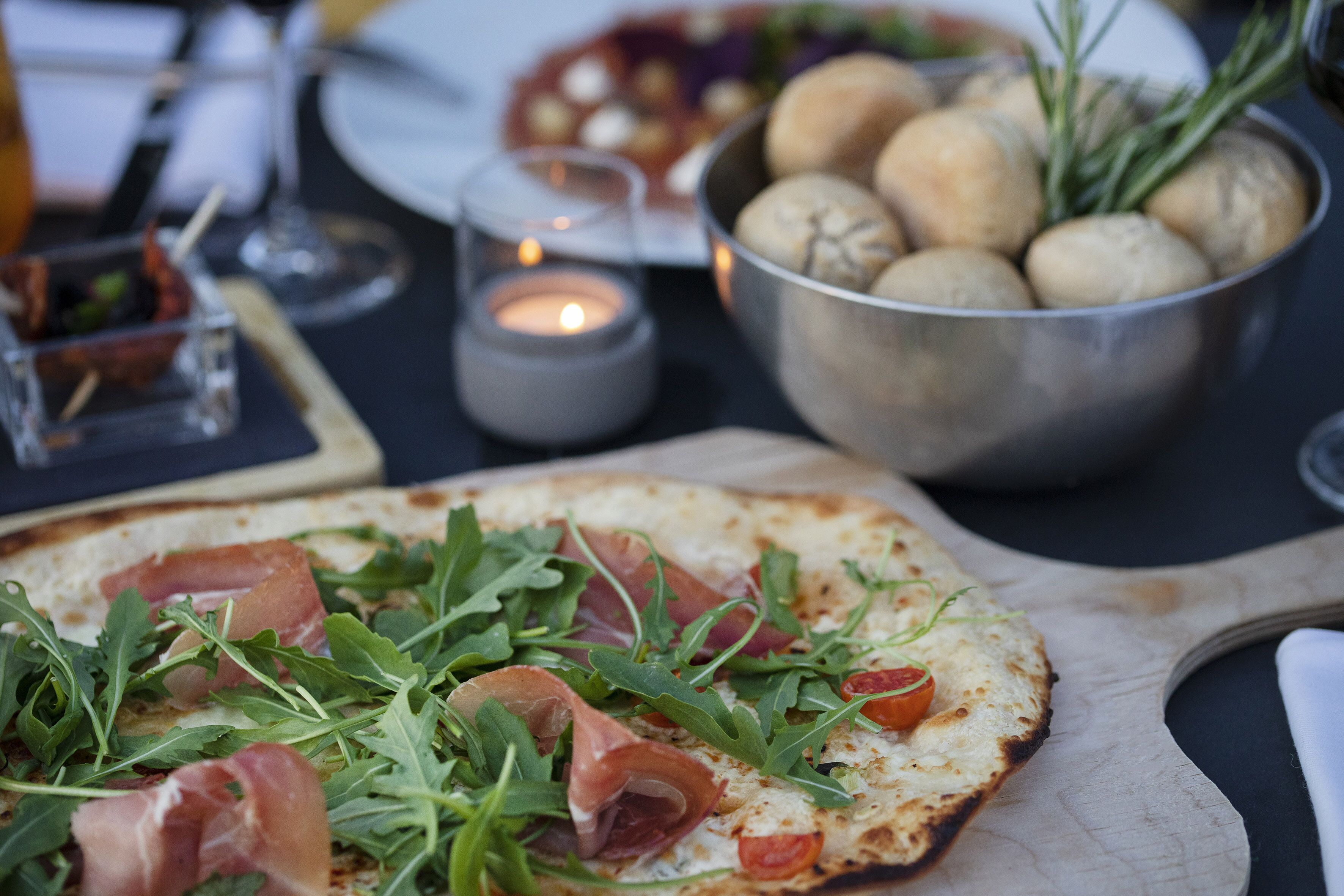A pizza with arugula and prosciutto on a wooden board.