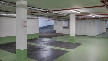 An indoor parking garage with concrete pillars, green and gray flooring, and red pipes on the ceiling.
