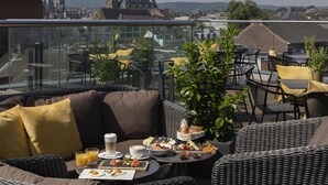Terraza en la azotea con mobiliario de mimbre, barandilla de cristal y vistas a la ciudad.