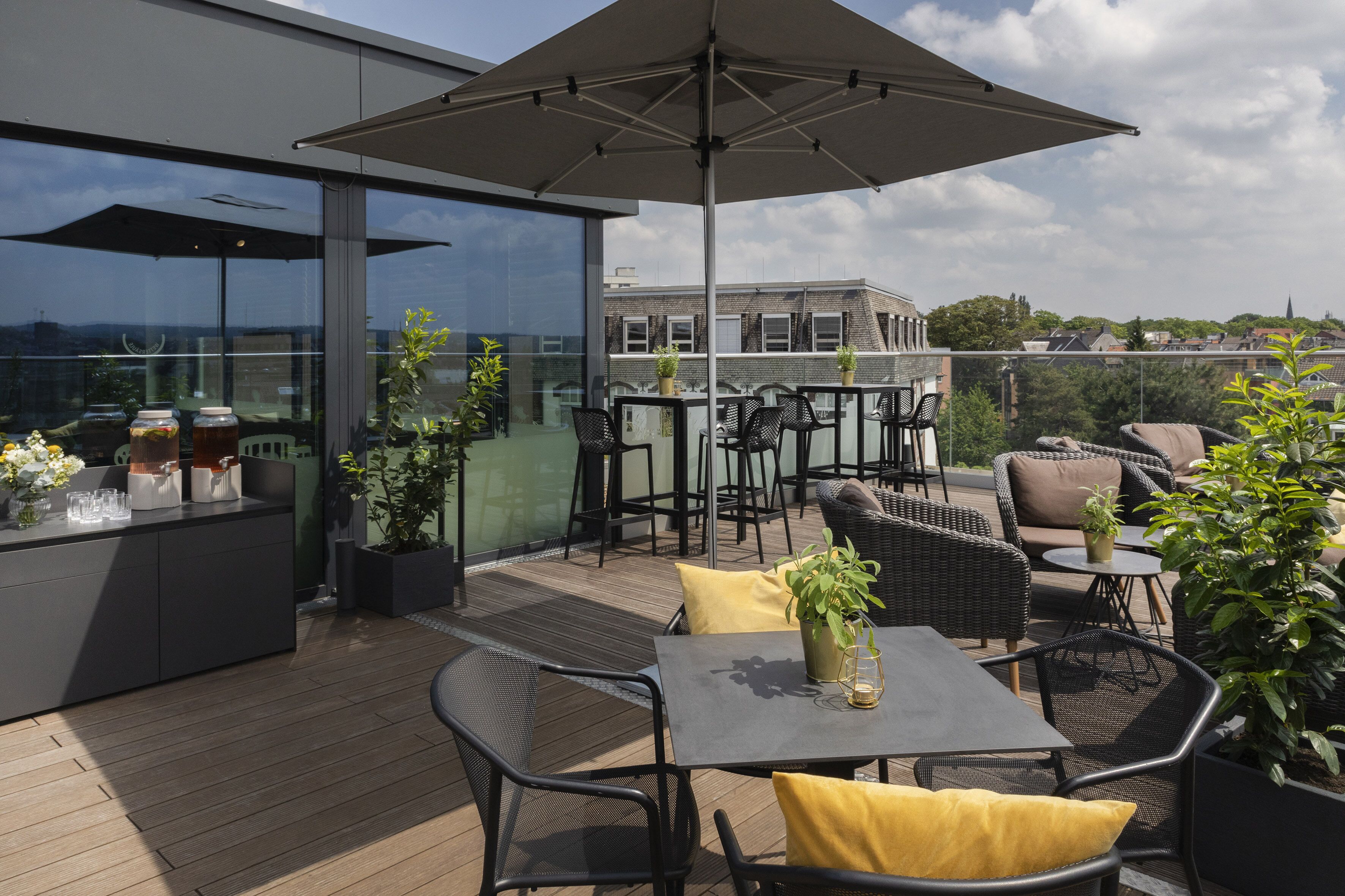 Een terras op het dak met buitenmeubels, een bar en potplanten.