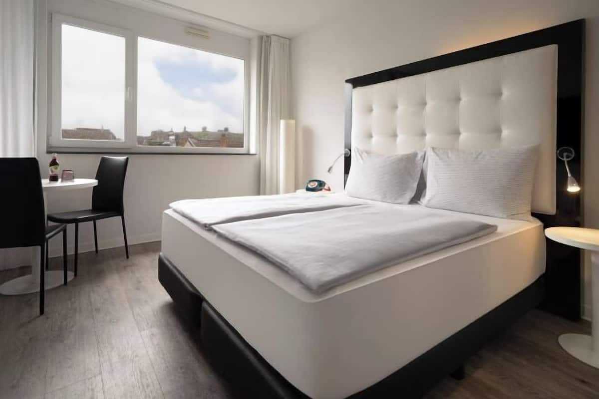 A hotel room with a large bed, a desk, and a chair.