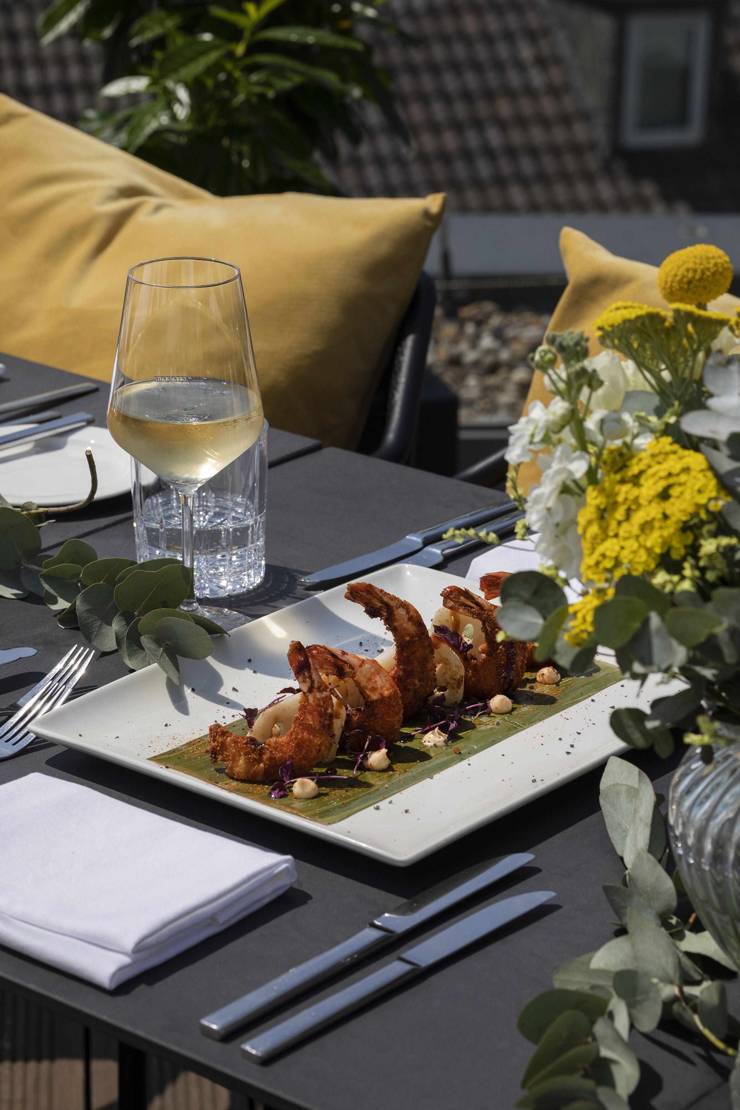 Een eettafel met een bord eten, bestek, een glas water en een vaas met bloemen.