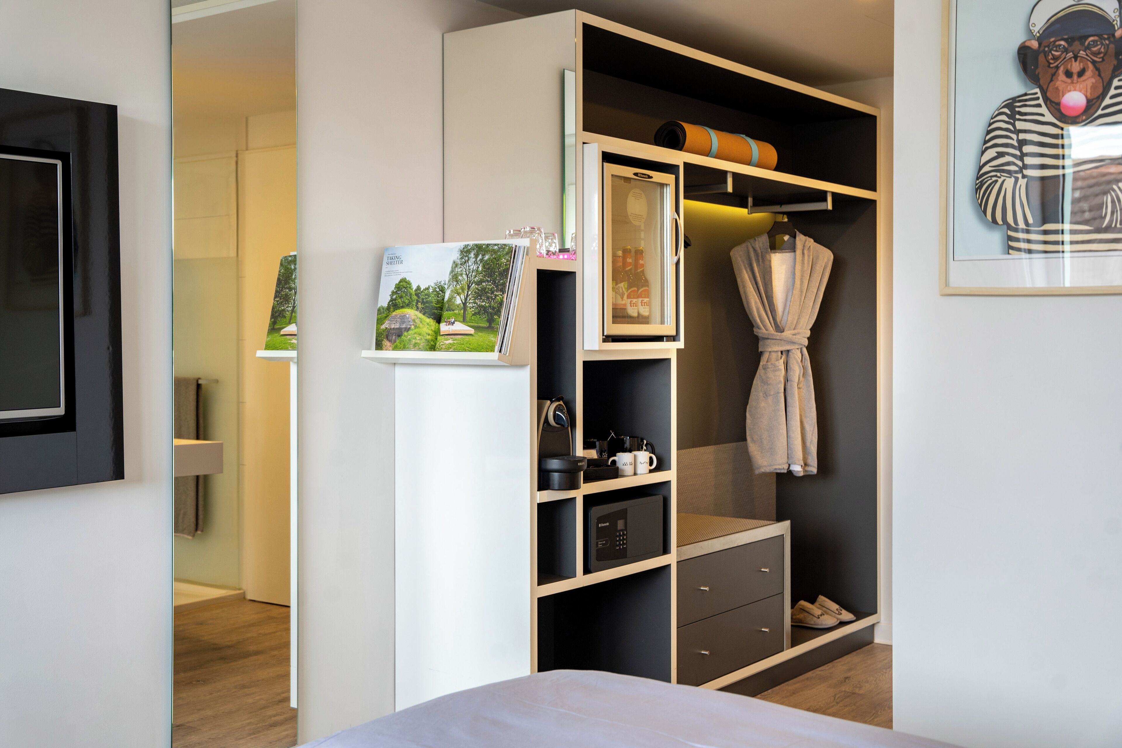 Een moderne slaapkamer met een bed, een garderobe met spiegel en een jas aan de deur.
