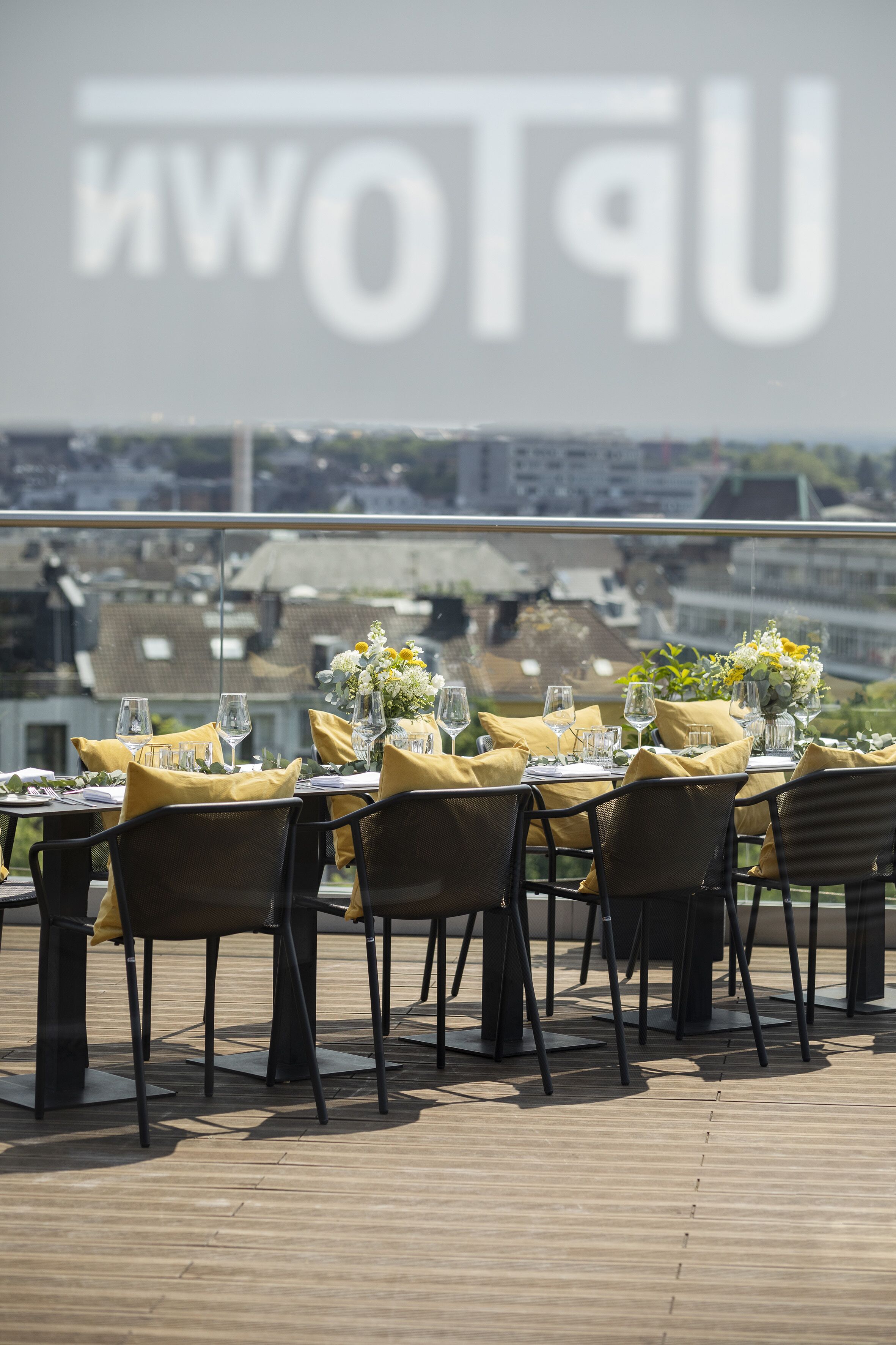 Comedor con mesas dispuestas para dos, con servilletas amarillas y cristalería, con vistas a un paisaje urbano.
