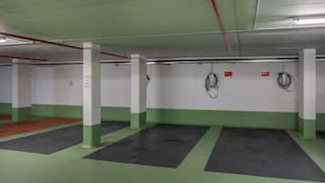 Un estacionamiento con marcas en el suelo verde y negro, pilares blancos y señales de salida rojas.