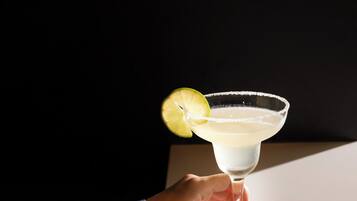 Eine Hand hält ein Cocktailglas mit Limettenscheibe auf einem Tisch.