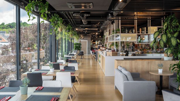 Un restaurante moderno con una barra larga, techos altos y amplios ventanales con vistas a un paisaje urbano.