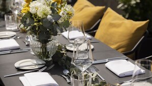 Una mesa servida para una comida, con un jarrón de flores, cristalería transparente y cubertería ordenada.