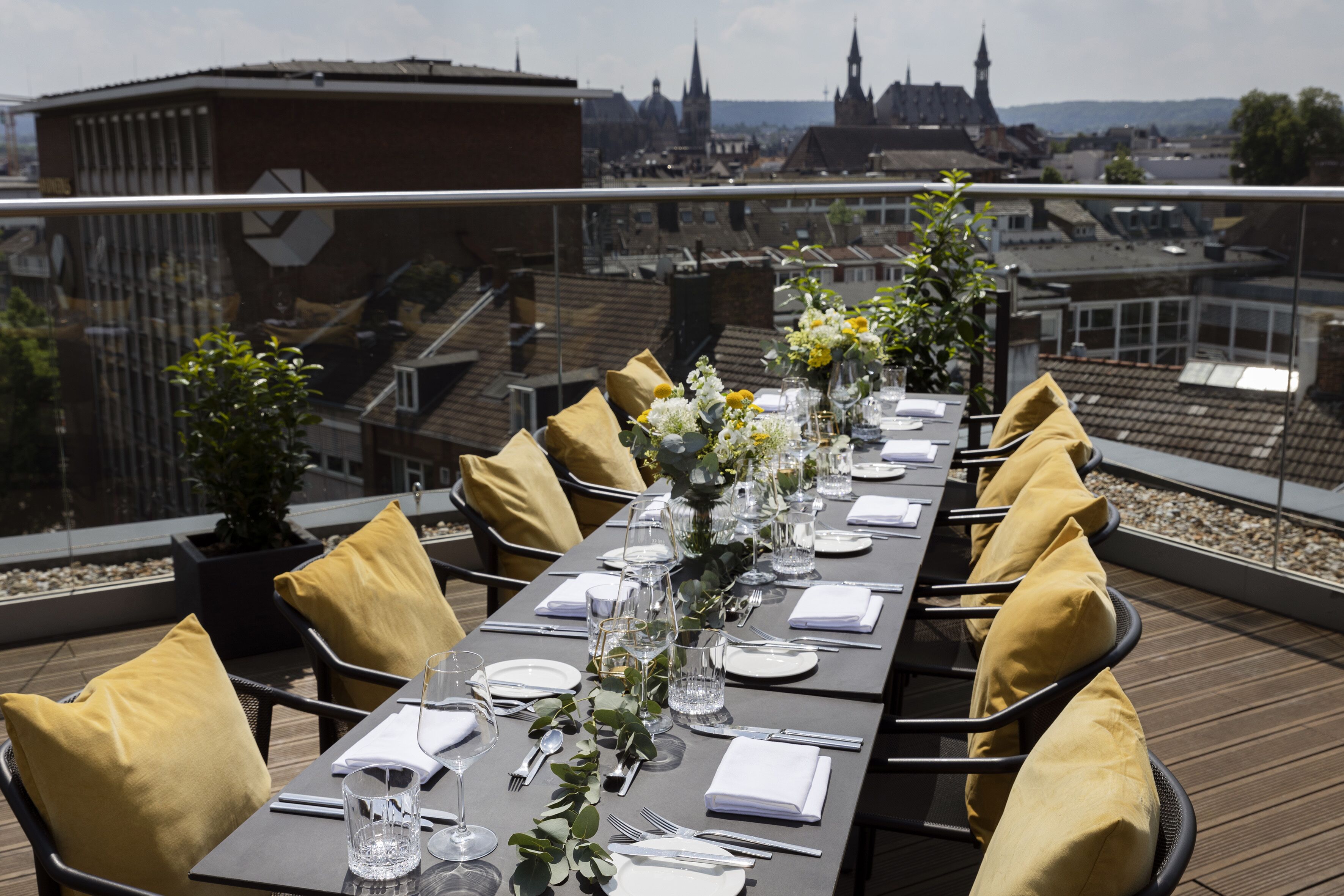 A rooftop dining area with tables set for a meal, overlooking a cityscape.