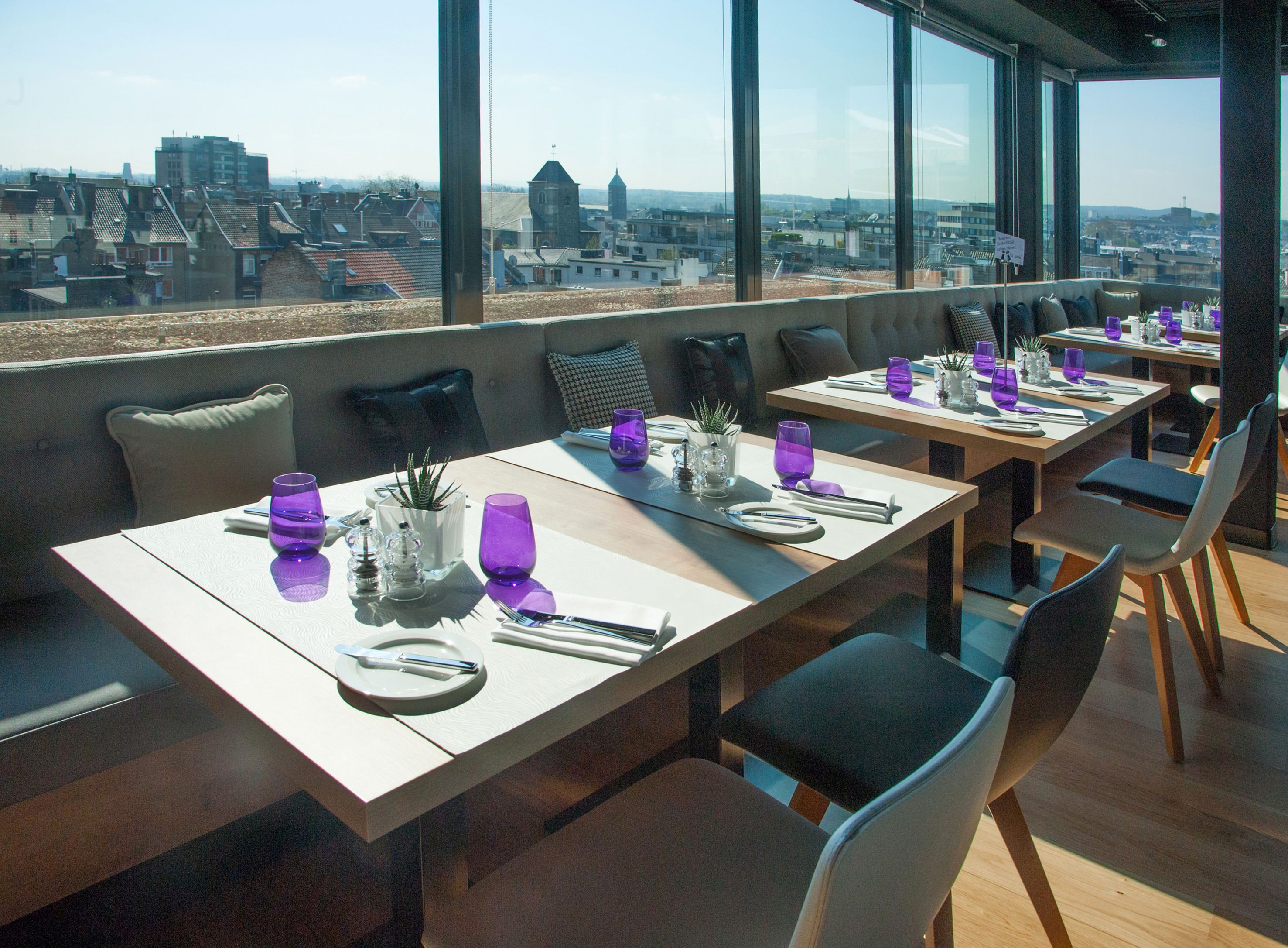A rooftop dining area with tables set for two, featuring purple glassware and white plates.