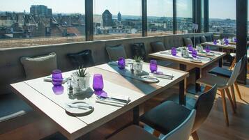 A rooftop dining area with tables set for two, featuring purple glassware and white plates.