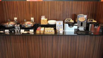Mostrador de buffet con diversos alimentos, incluyendo gofres, y una estación de café con varias cafeteras.