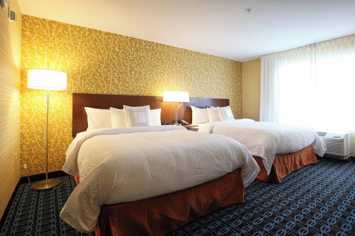A hotel room with two beds, a patterned wall, and a large window with curtains.