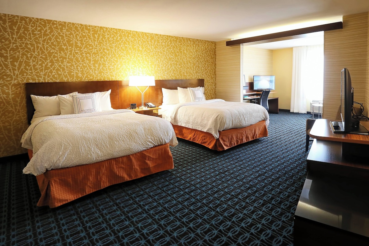 A hotel room with two beds, a desk, a television, and a large window.