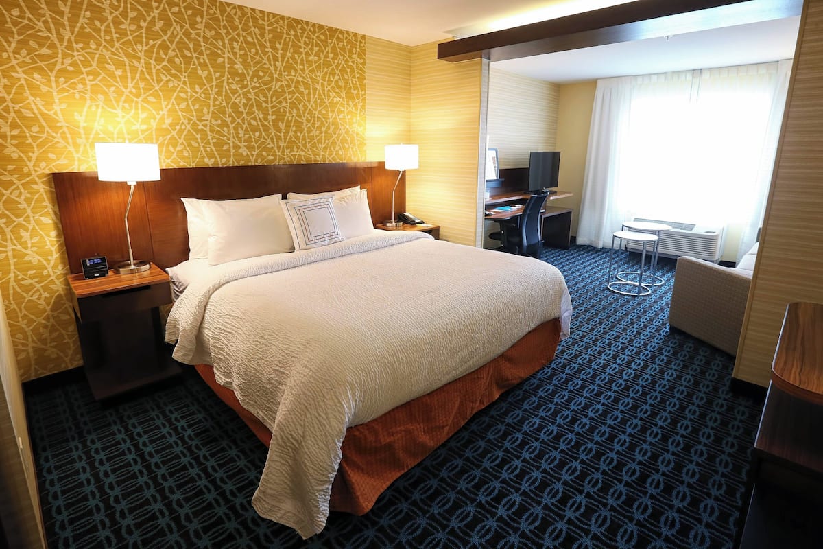 A hotel room with a large bed, two bedside tables with lamps, a desk with a chair, and a large window with curtains.