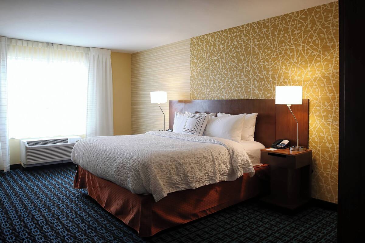 A hotel room with a bed, bedside lamps, a telephone, and a wall air conditioner.