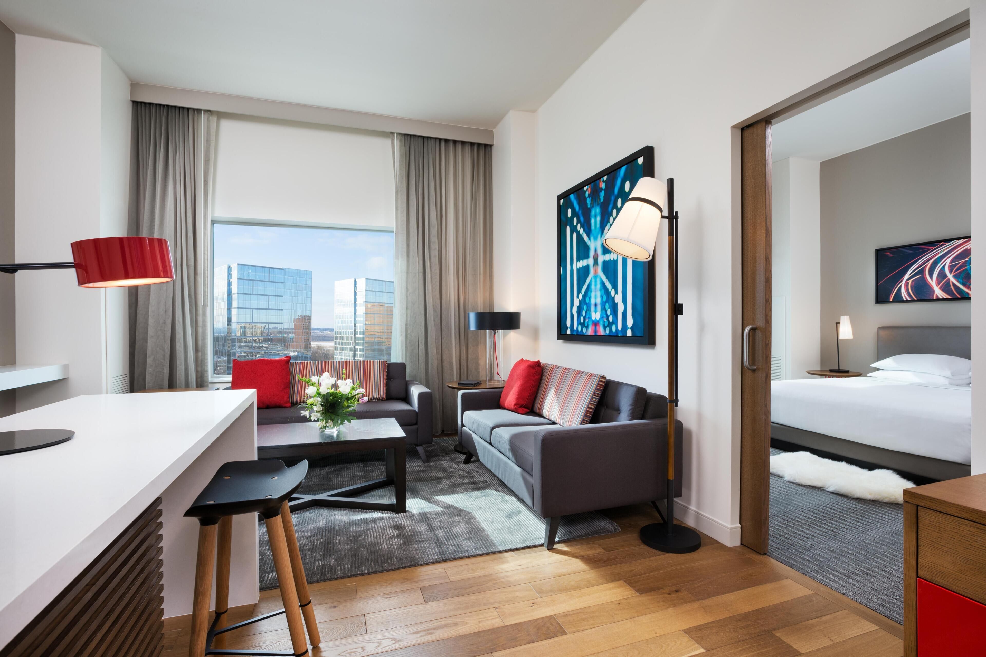 A modern hotel room with a desk, sofa, and bed.