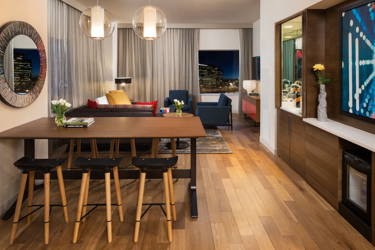 Uma sala de estar moderna com uma mesa de jantar de madeira, banquetas de bar, um sofá e uma televisão.