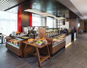 Una barra de desayuno moderna con diversas opciones de comida, una máquina de café y un área de estar con vista a la cocina.