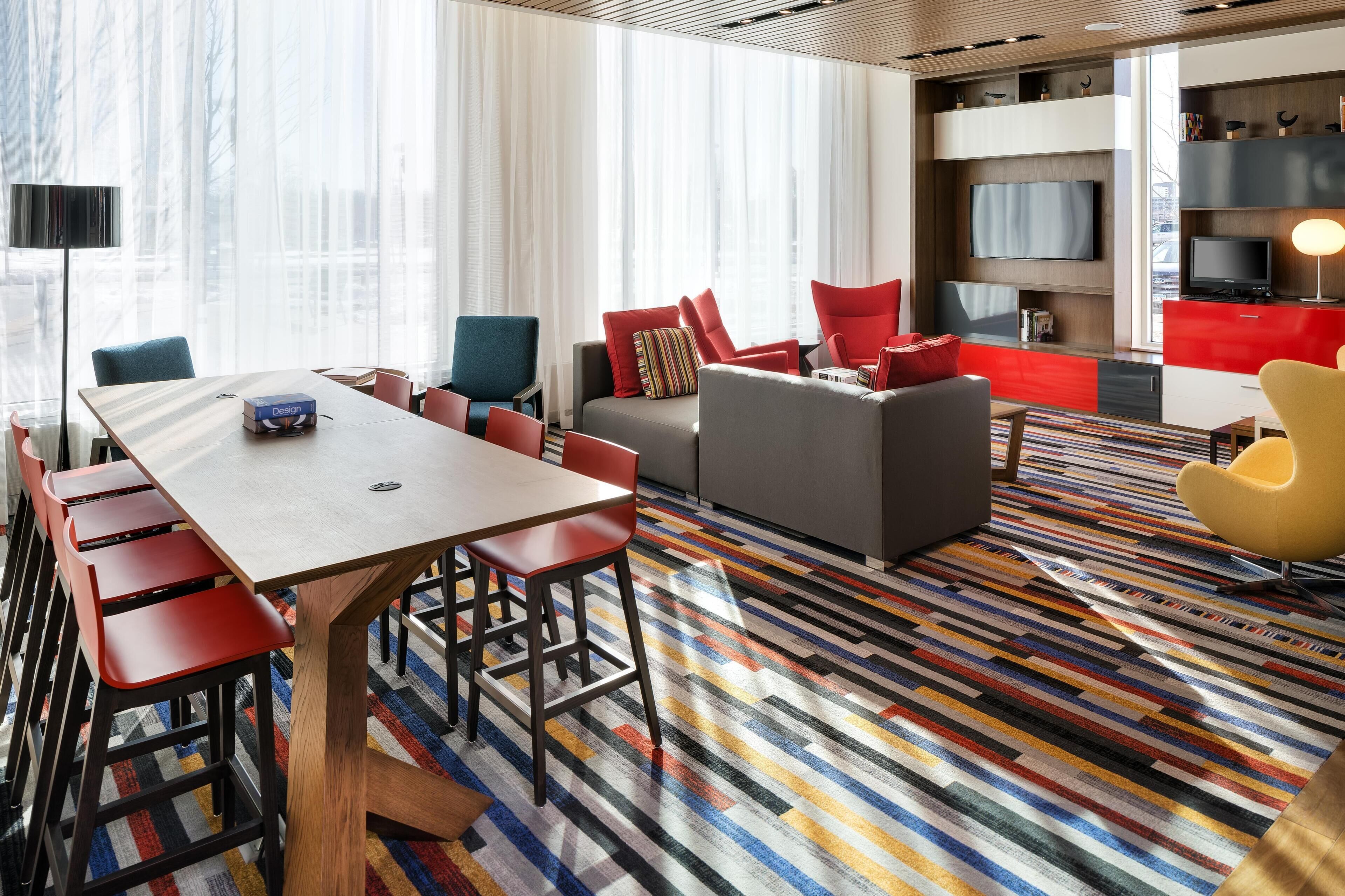 A modern hotel room with a dining area, a sofa set, and a television.