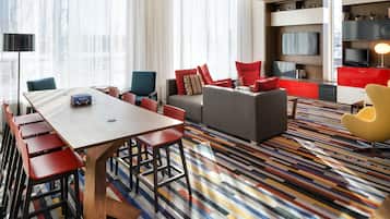 A modern hotel room with a dining area, a sofa set, and a television.