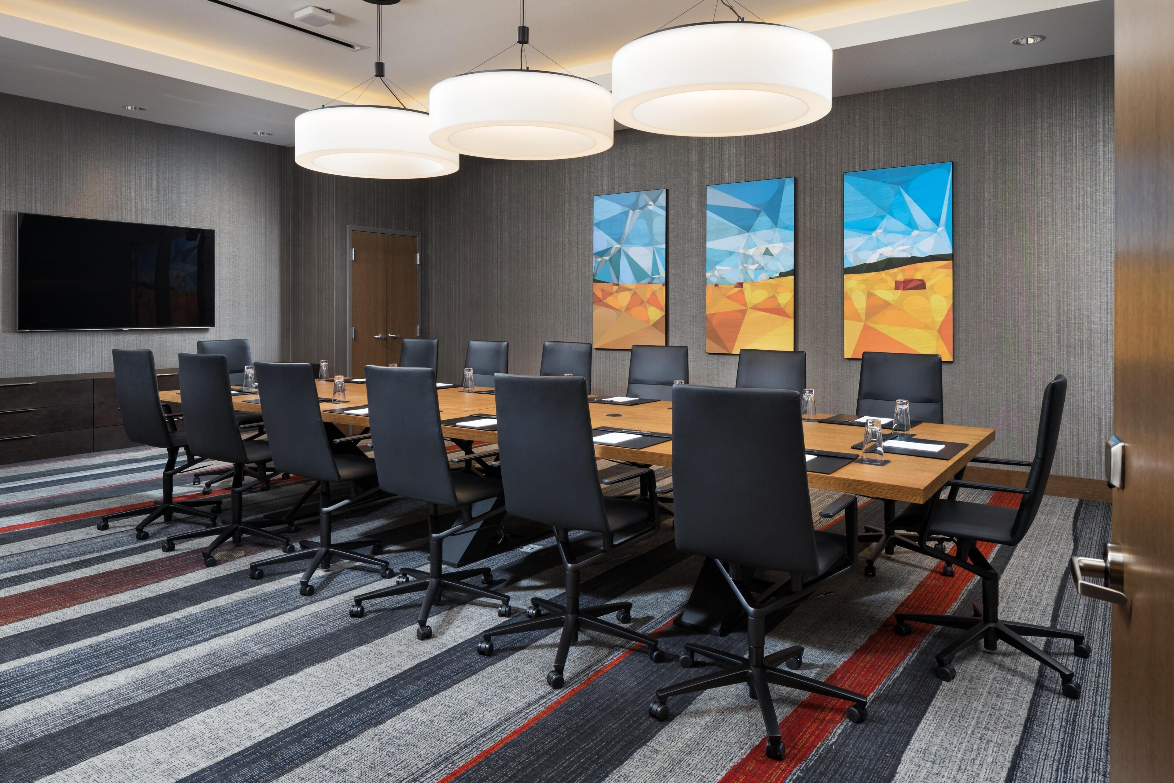 A conference room with a long table, multiple chairs, and a large flat-screen TV.
