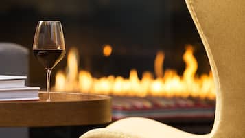 Una poltrona gialla con un bicchiere di vino rosso su un tavolino di legno, sullo sfondo sfocato di un camino.