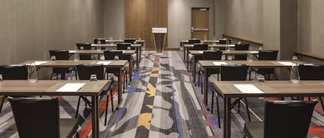 A conference room with multiple tables and chairs, a carpeted floor, and a door at the far end.