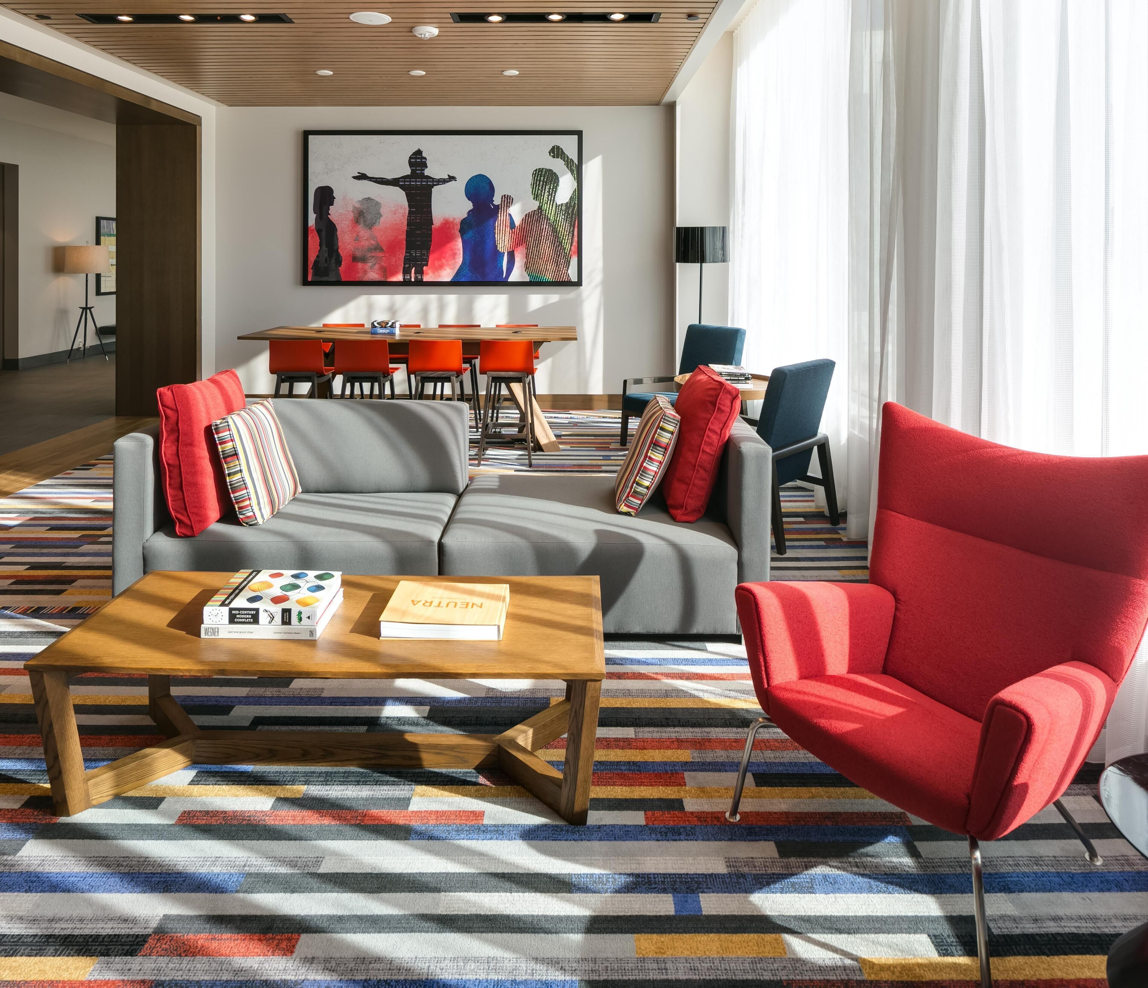 A modern living room with a sofa, a red armchair, a coffee table with books, and a colorful striped rug.
