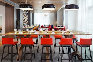 Uma zona de refeições moderna com uma mesa comprida, cadeiras vermelhas e luminárias pendentes pretas.