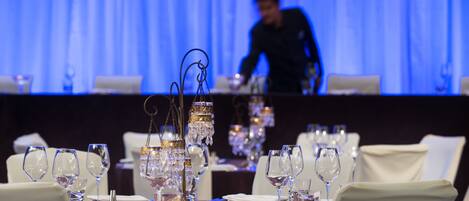 Una mesa de comedor dispuesta con varias copas de vino, un centro de mesa y un camarero al fondo.