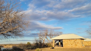 Un edificio de piedra con un patio cubierto, rodeado de paisaje natural y árboles.