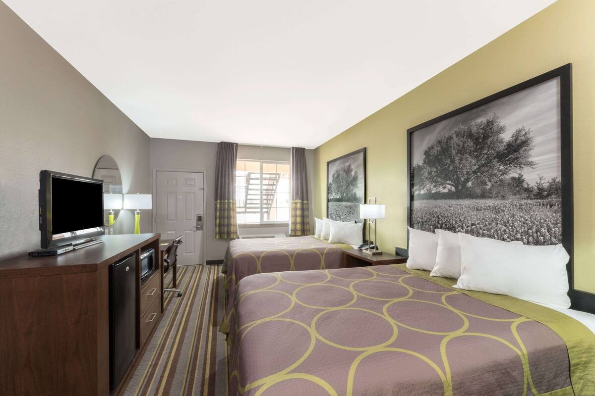 A hotel room with two beds, a TV, a desk, and a window with curtains.