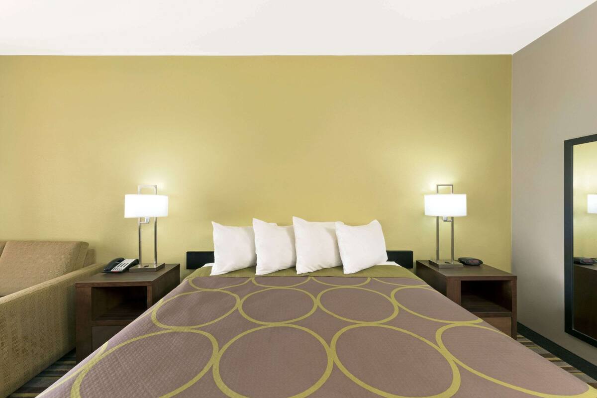 A hotel room with a bed, two bedside tables with lamps, a chair, and a large mirror on the wall.