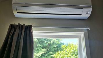 Une pièce dotée d’un climatiseur fixé au mur, au-dessus d’une fenêtre donnant sur un paysage verdoyant.