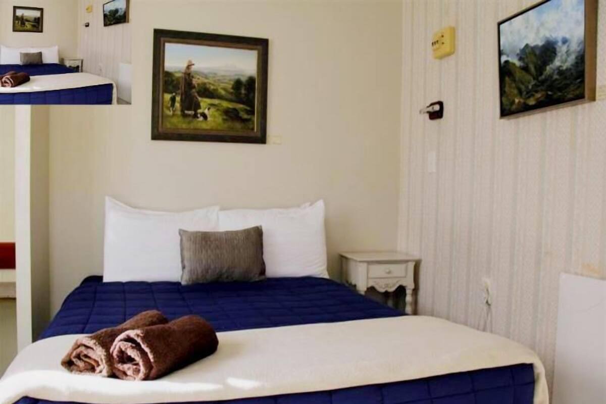 Ett hotellrum med en säng, ett nattduksbord, en tavla och en väggmonterad ljusströmbrytare.