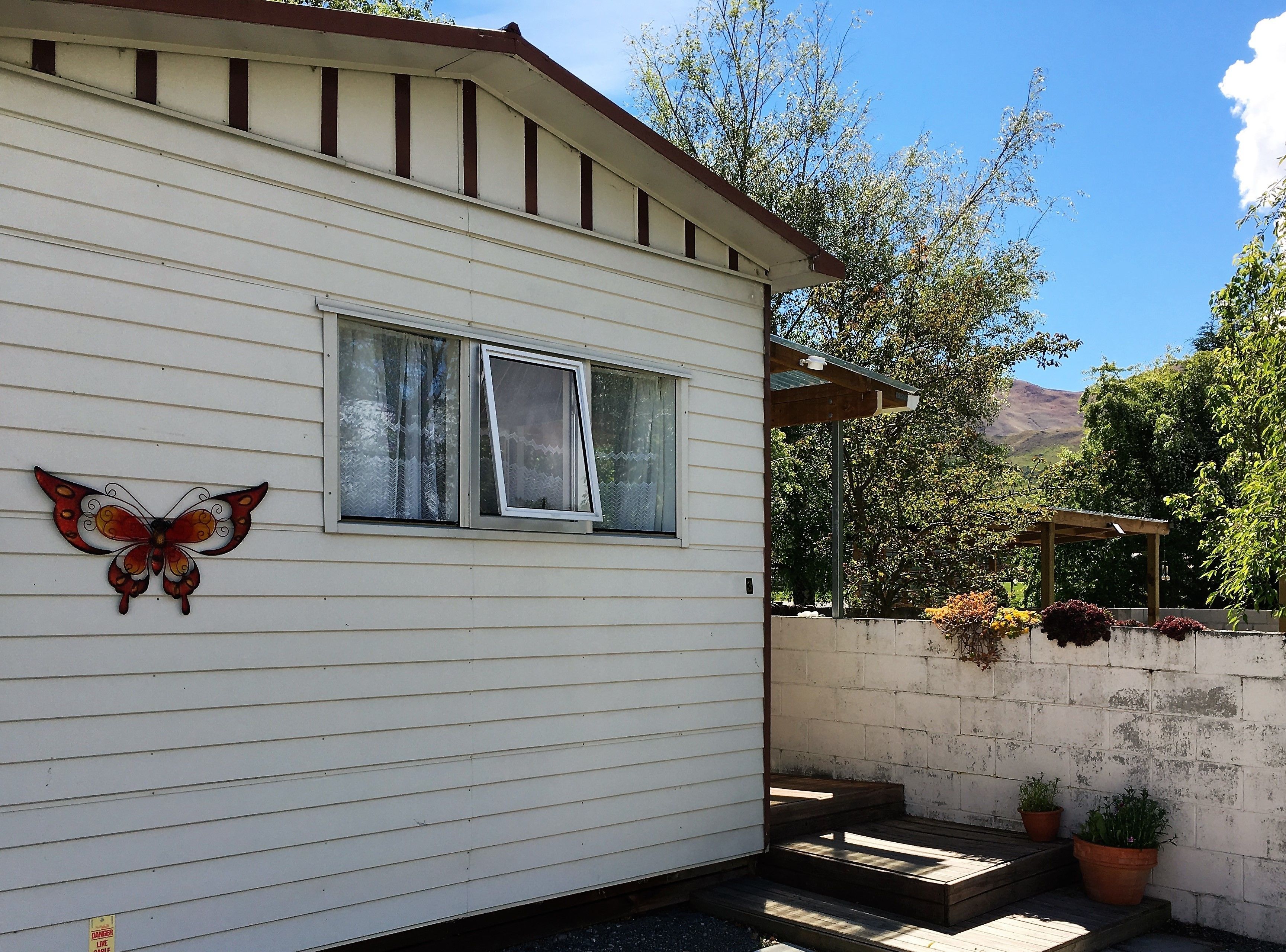 Una casa blanca con un adorno de mariposa, una ventana y una pérgola de madera con plantas en macetas.