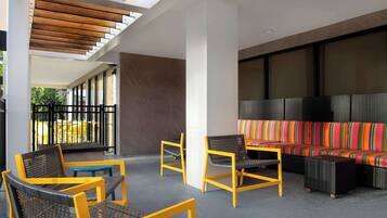 A covered outdoor seating area with wicker chairs and a colorful sofa, a blue table, and a view of the outside.