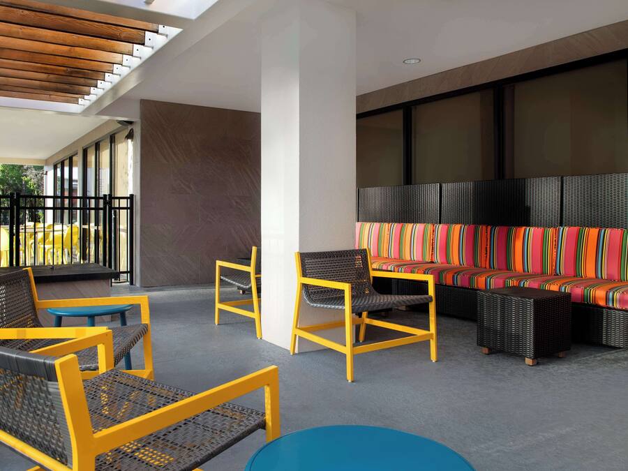 A covered outdoor seating area with wicker chairs and a colorful sofa, a blue table, and a view of the outside.