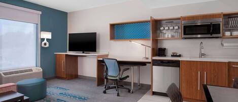 A modern kitchen with a microwave, stove, and dishwasher. There is a dining table with chairs and a small office area with a desk and chair.