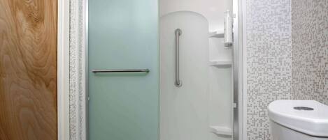 A bathroom with a shower, toilet, and a glass door.