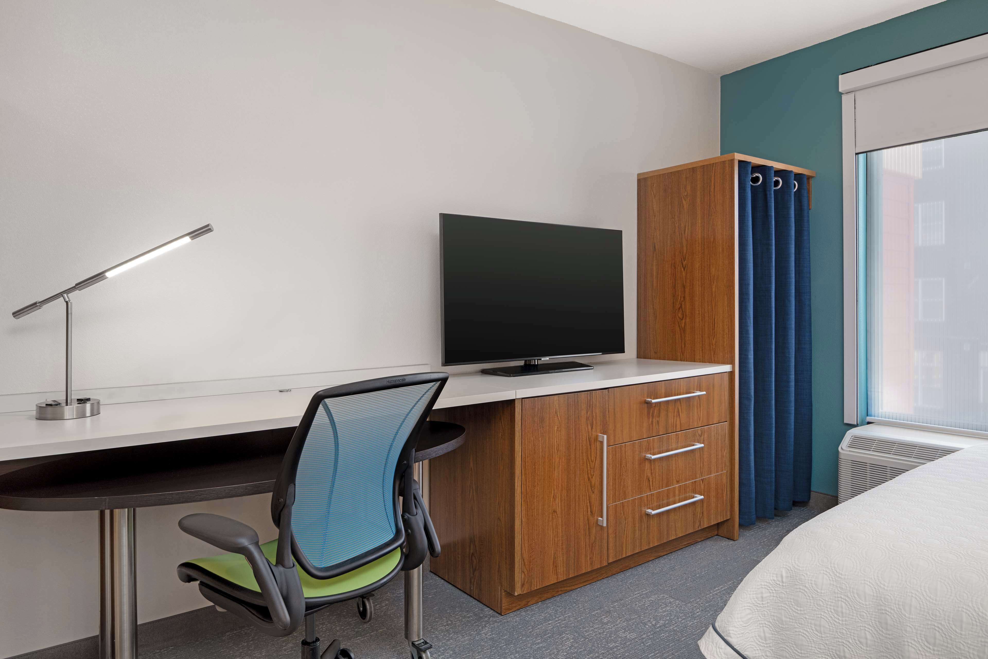 Habitación de hotel con escritorio, silla, televisor, armario y cama.